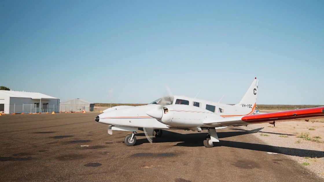 A light plane sitting on the tarmac with a shed in the background.