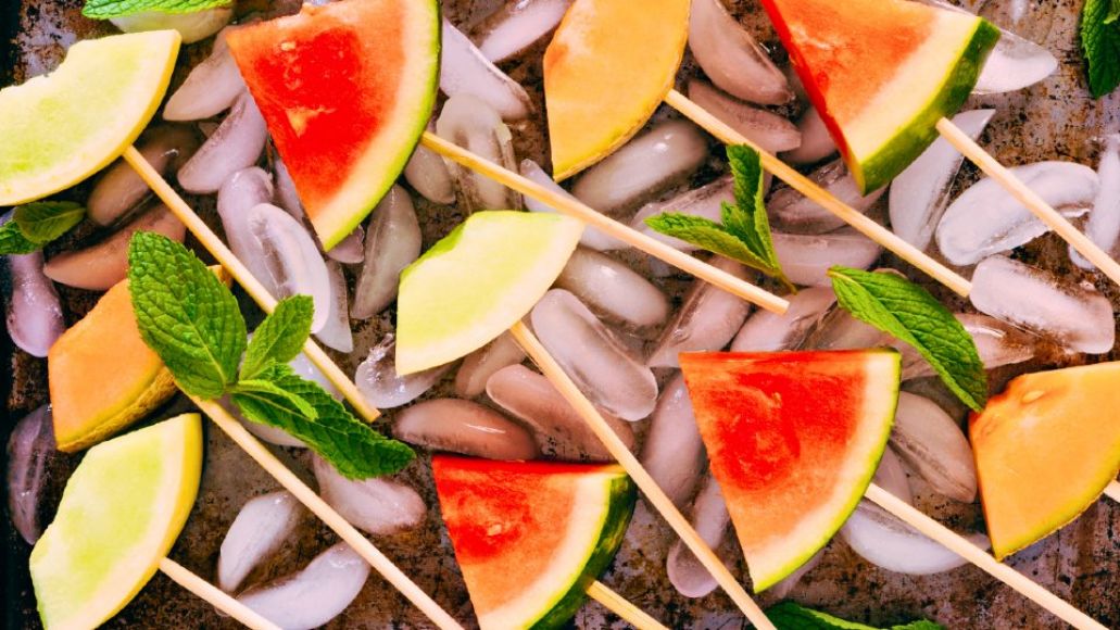 Pieces of melon on sticks resting on ice cubes with sprigs of mint