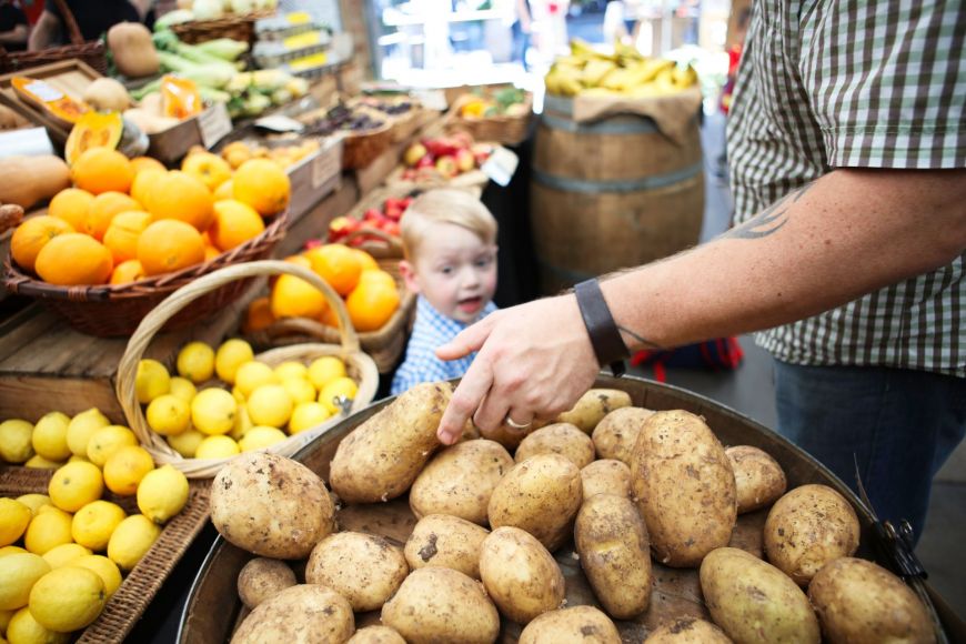 Shelves of fresh produce, and a person's arm reaching for potatoes.